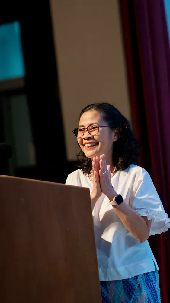 A woman is standing at a podium clapping her hands and smiling.