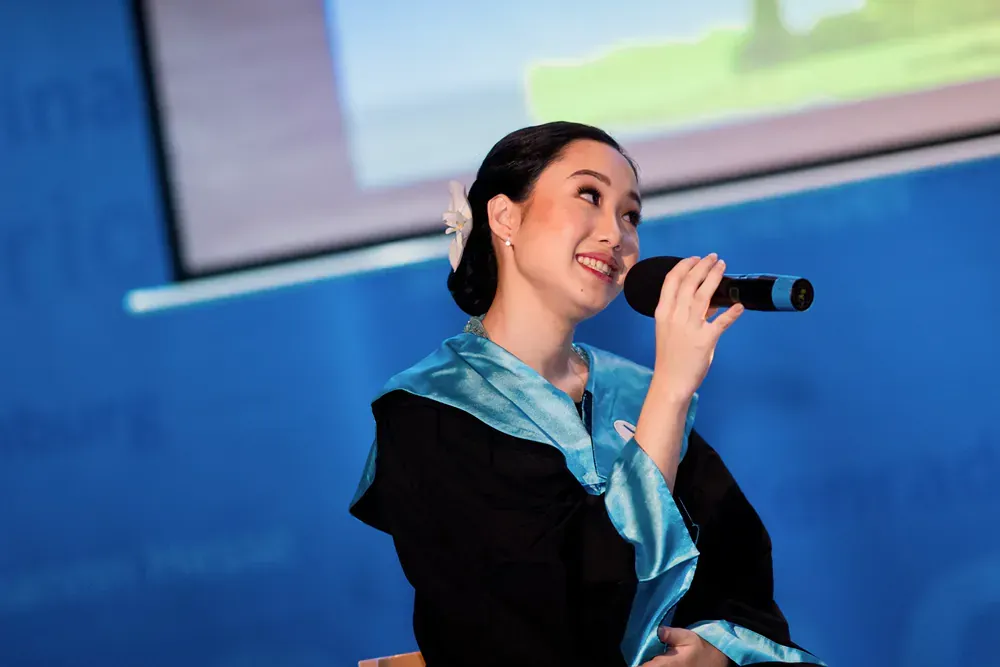 A woman in a graduation cap and gown is singing into a microphone.