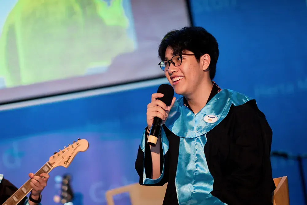 A man in a graduation cap and gown is holding a microphone and playing a guitar.