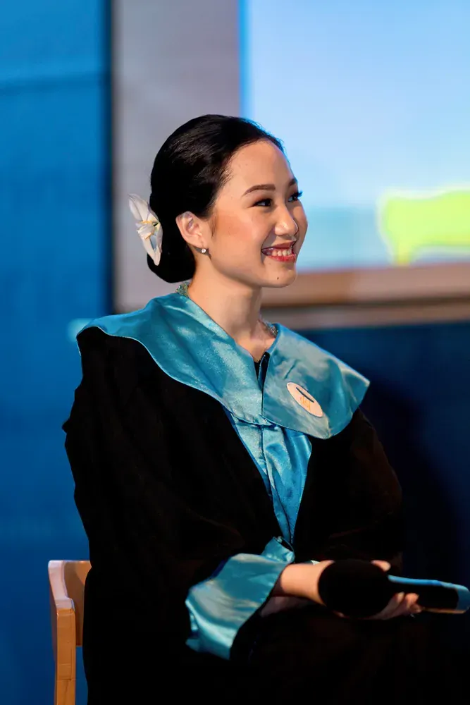 A woman in a graduation gown is sitting in a chair and smiling.