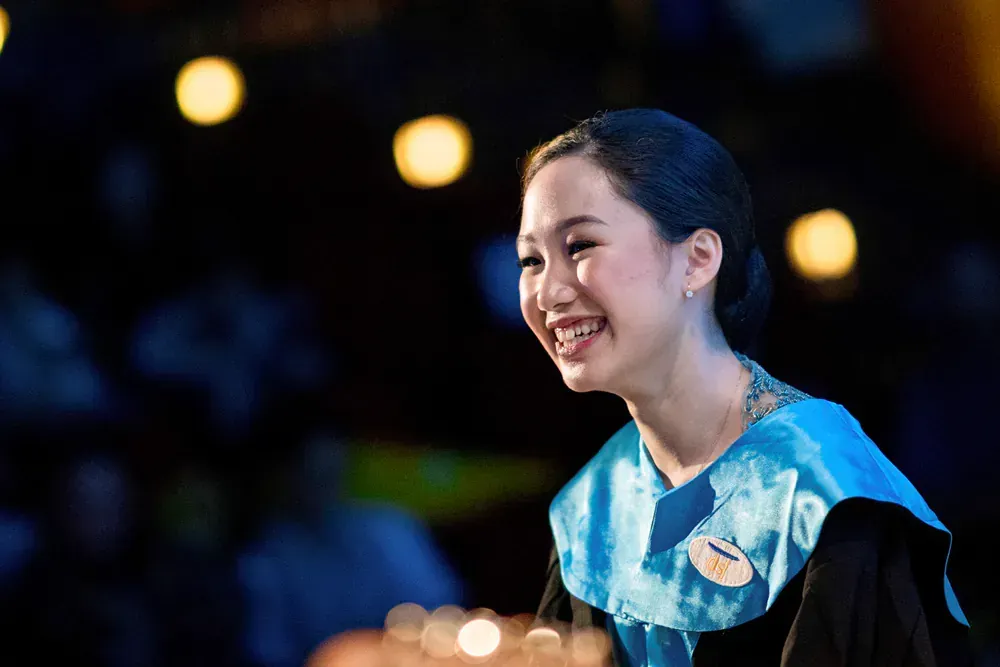 A woman in a graduation cap and gown is smiling.