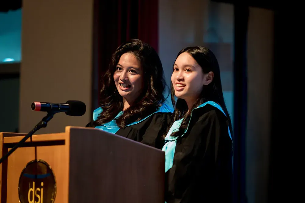 Two female graduates are standing at a podium giving a speech.