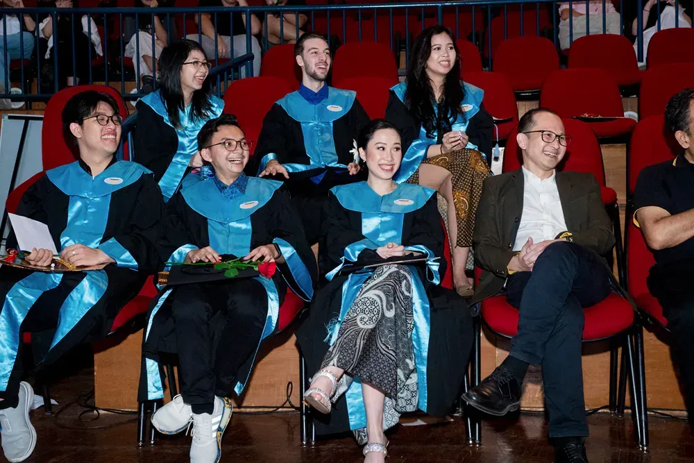 A group of graduates are sitting in red chairs in an auditorium.