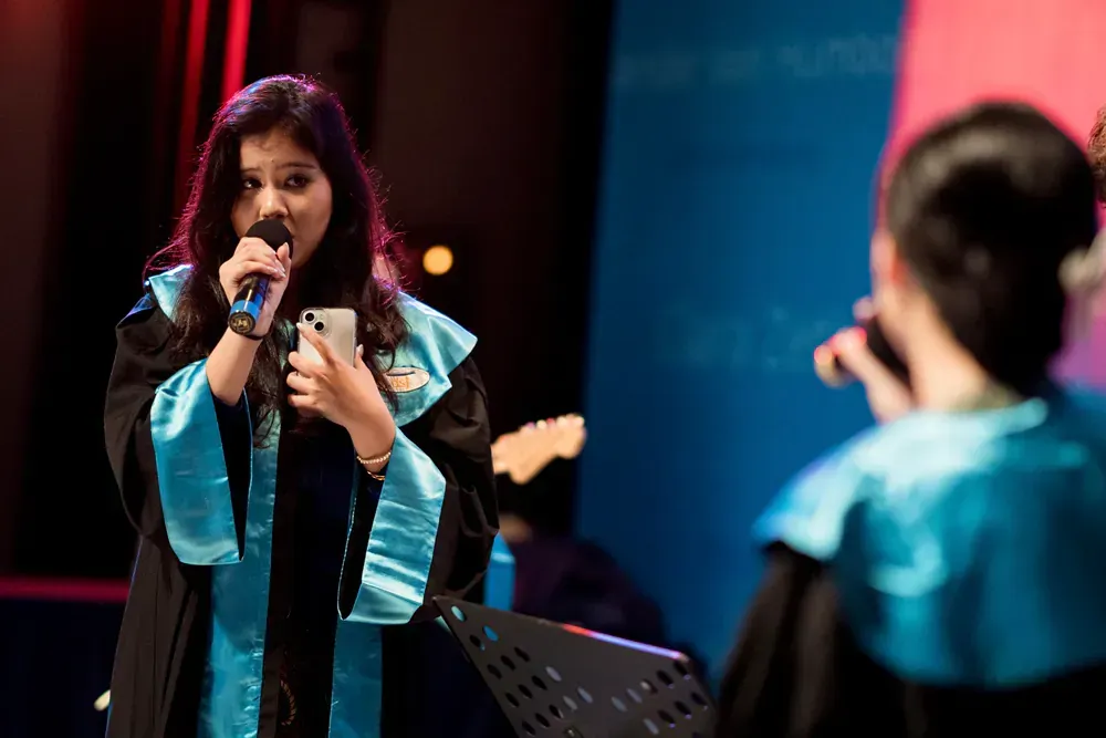 A woman in a graduation gown is singing into a microphone.