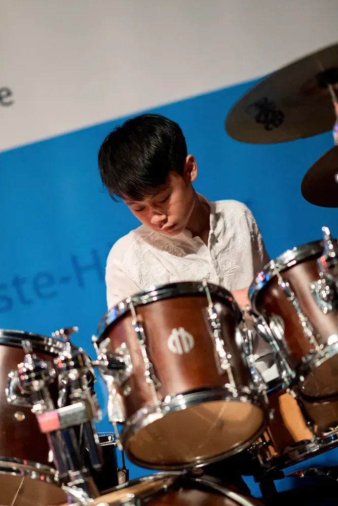 A young man is playing drums in front of a sign that says ste-h