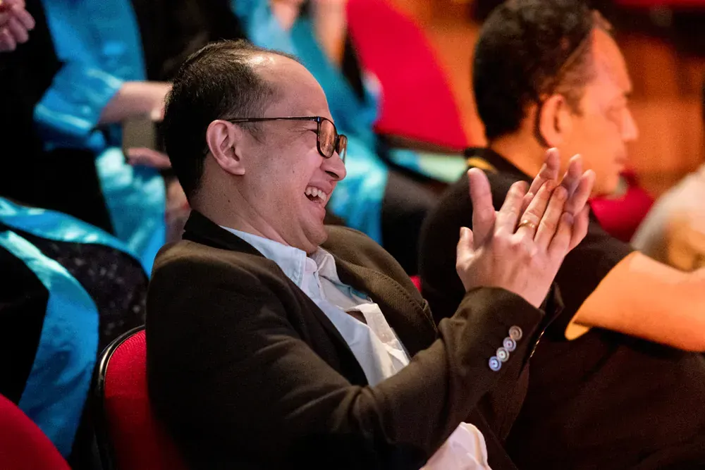 A man in a suit is laughing while sitting in a theater.