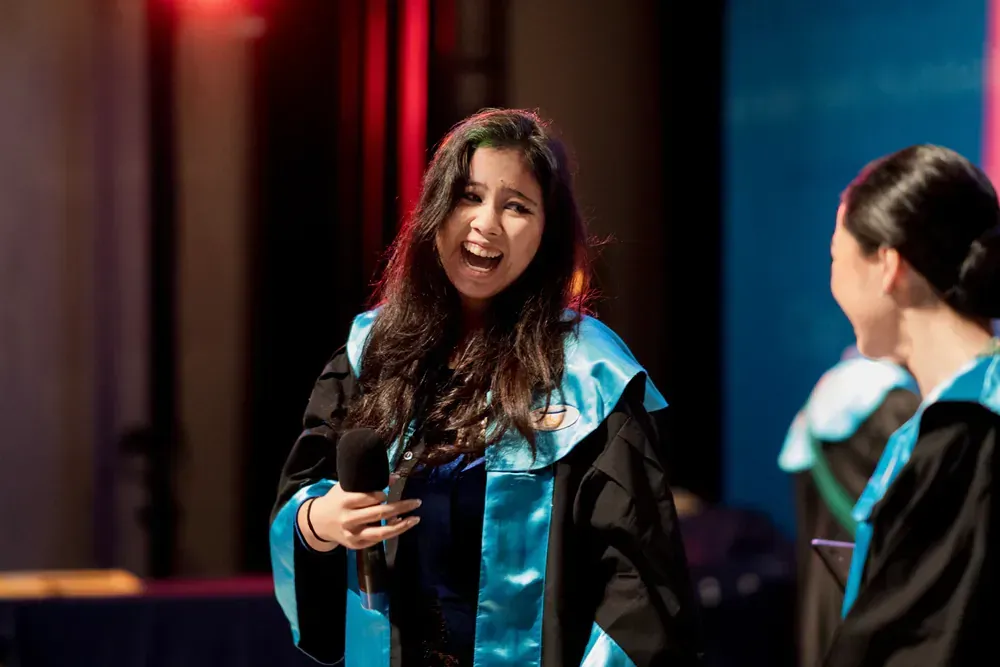 A woman in a graduation gown is laughing while standing next to another woman.