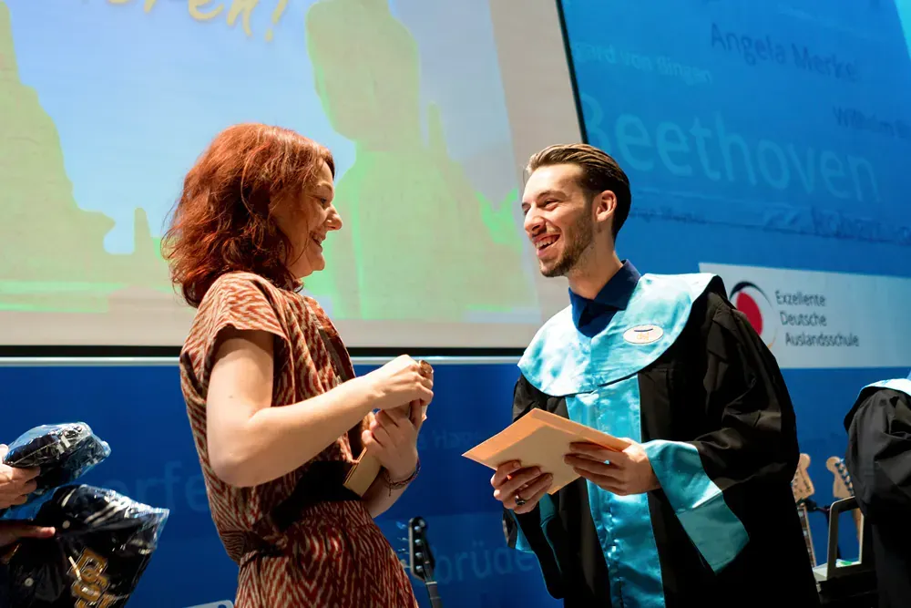 A man in a graduation gown is talking to a woman