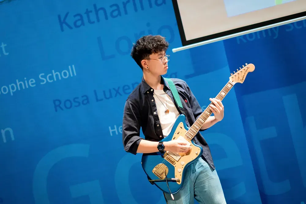 A young man is playing an electric guitar in front of a blue wall.