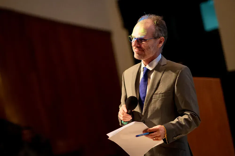 A man in a suit and tie is holding a microphone and a piece of paper.