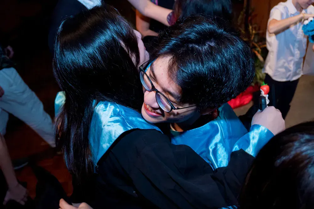 A man in a graduation cap and gown is hugging a woman in a crowd.
