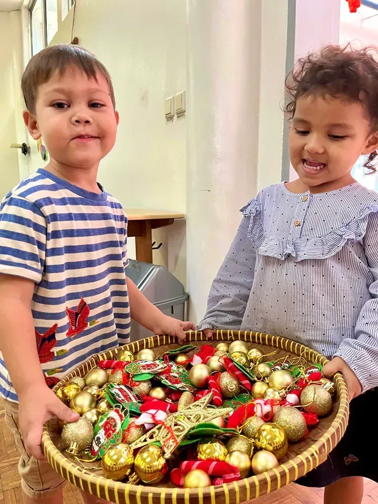 A boy and a girl are holding a basket of christmas decorations.