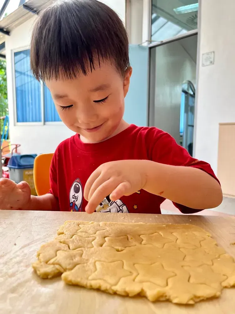 A young boy is sitting at a table cutting dough into shapes.