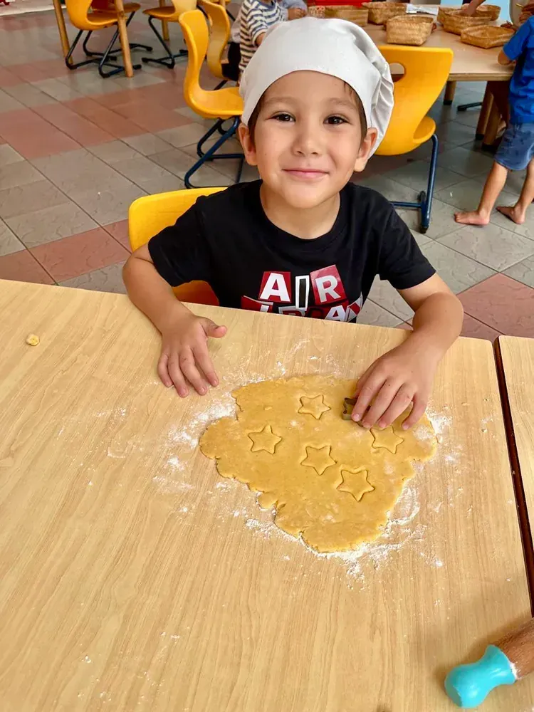 A young boy wearing a chef hat is sitting at a table making cookies