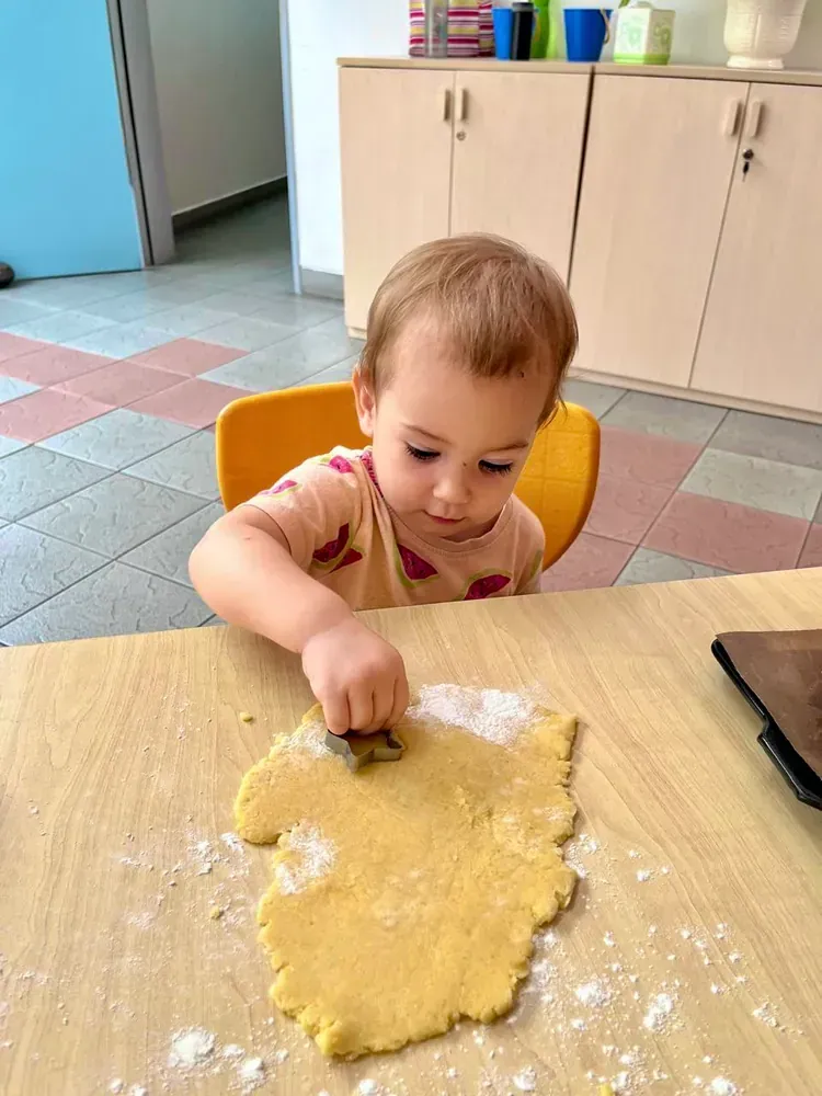 A little girl is sitting at a table cutting dough into shapes.