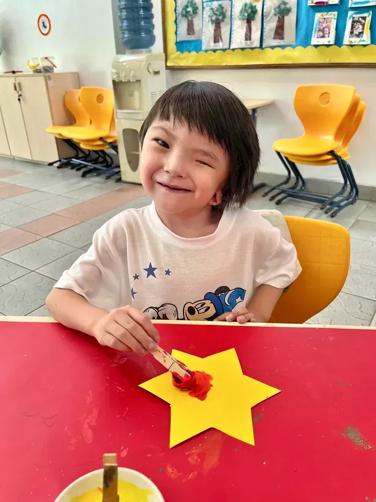 A little girl is sitting at a table painting a yellow star.