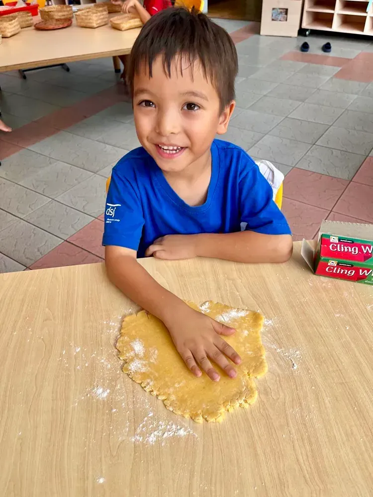 A young boy is sitting at a table with a piece of dough on it.