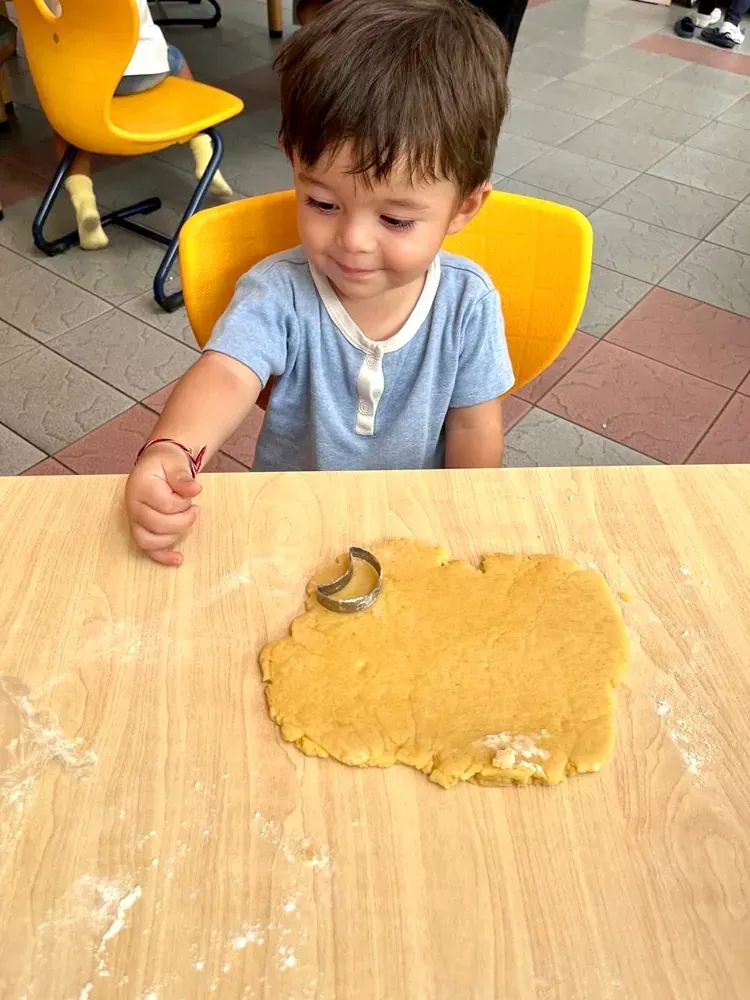A little boy is sitting at a table cutting dough with a cookie cutter.