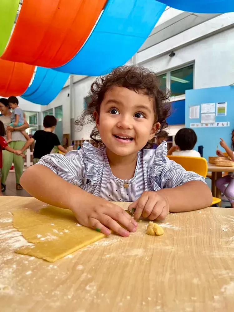 A little girl is sitting at a table with a piece of dough on it.