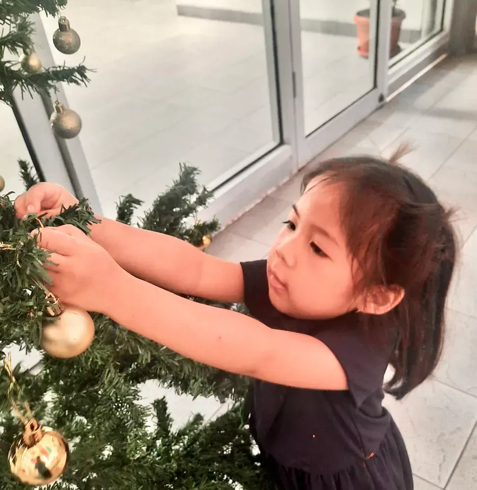 A little girl in a black dress decorates a christmas tree