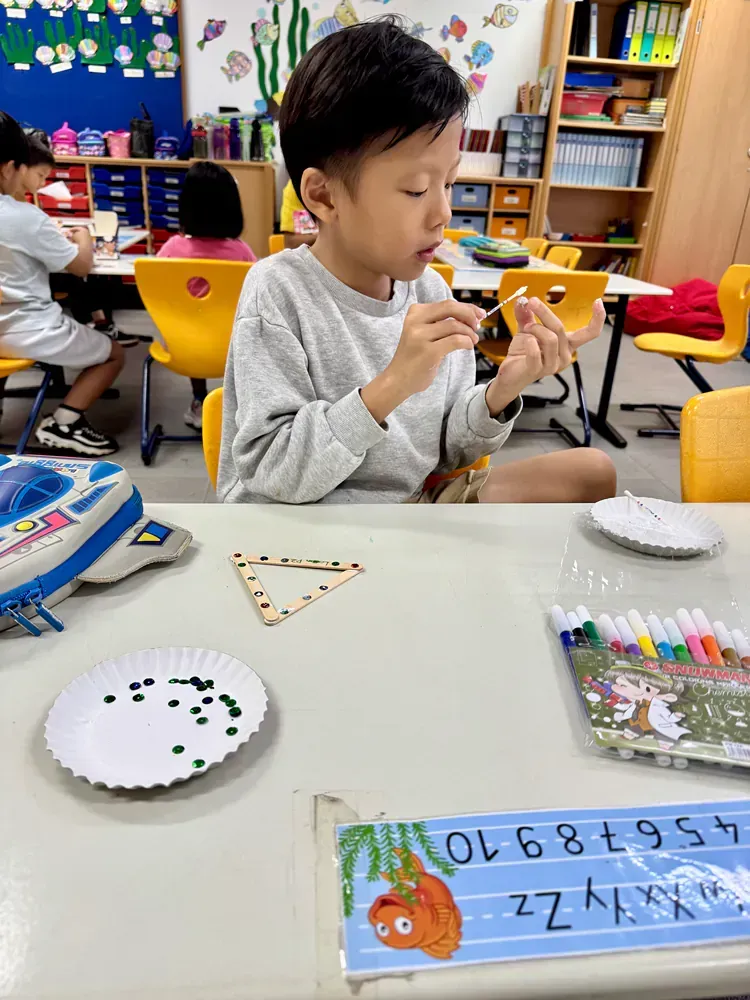 A young boy is sitting at a table in a classroom eating a snack.