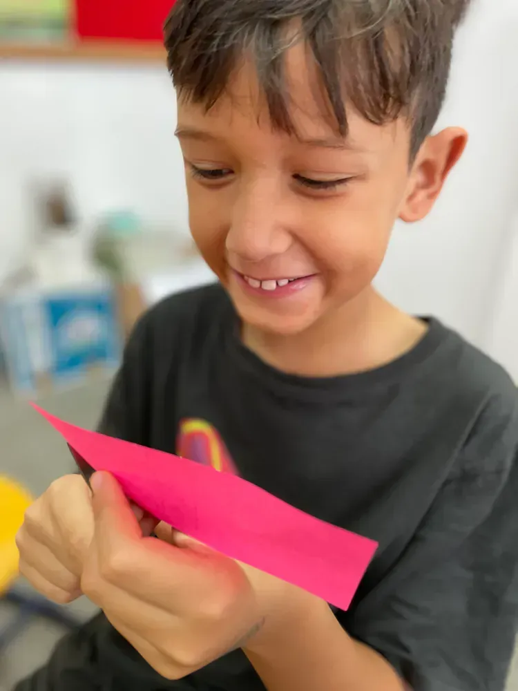 A young boy is smiling while holding a piece of pink paper
