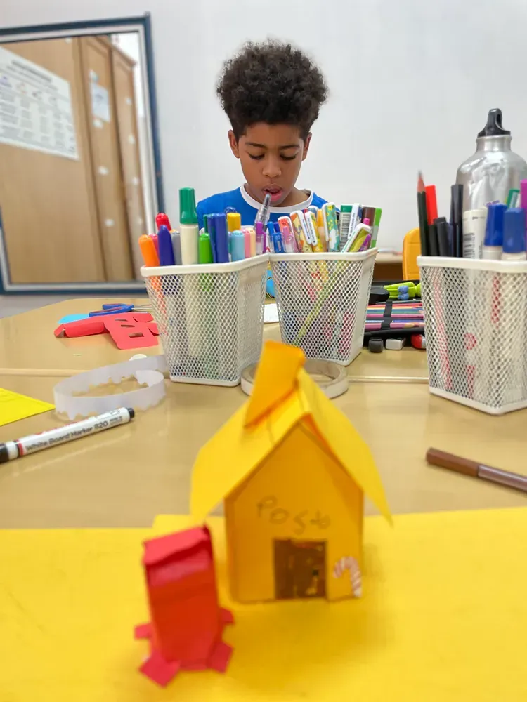 A boy is sitting at a table with a yellow house and a red mailbox
