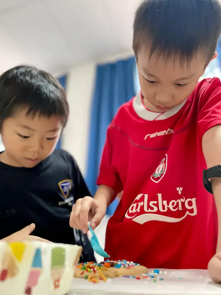 A boy wearing a red carlsberg shirt is cutting a cake