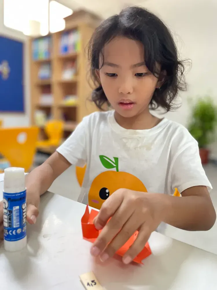 A little girl is sitting at a table with a bottle of glue