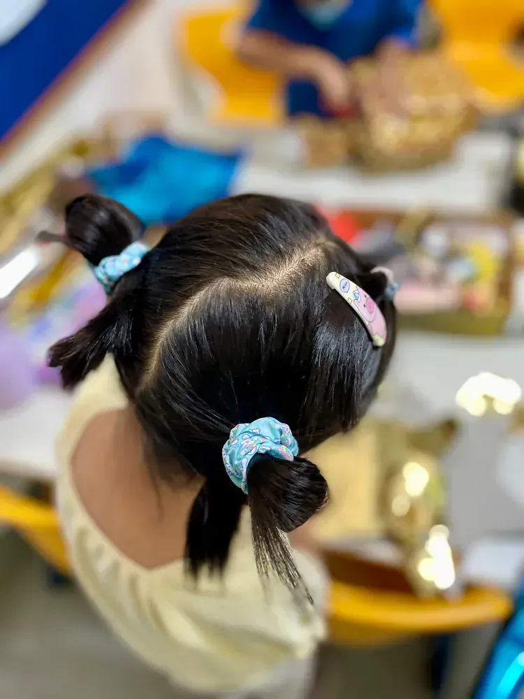 A little girl is sitting at a table with a bun in her hair.