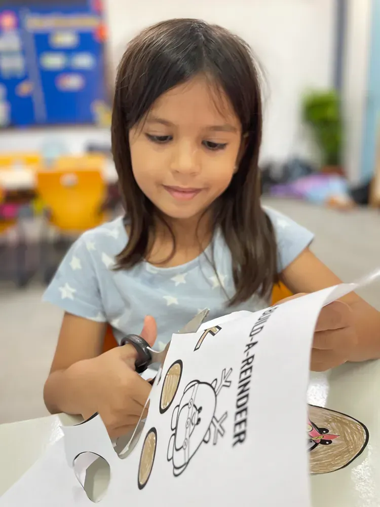A little girl is cutting a piece of paper with scissors.