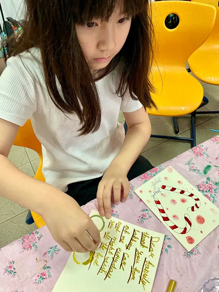 A little girl is sitting at a table writing on a piece of paper.