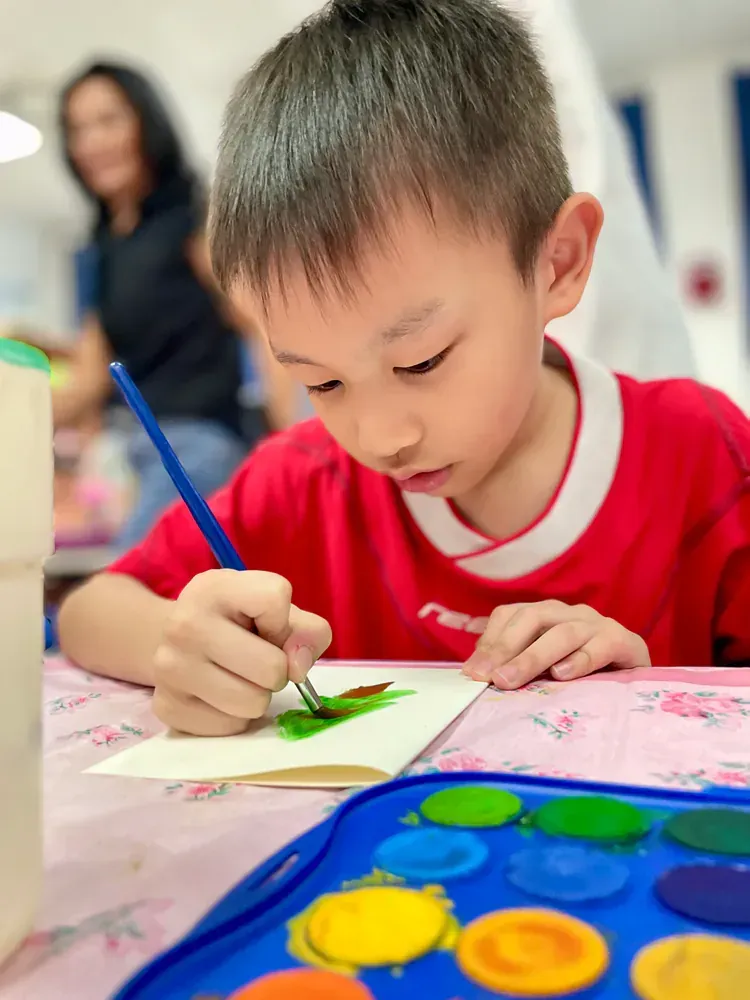 A young boy in a red shirt is painting with watercolors