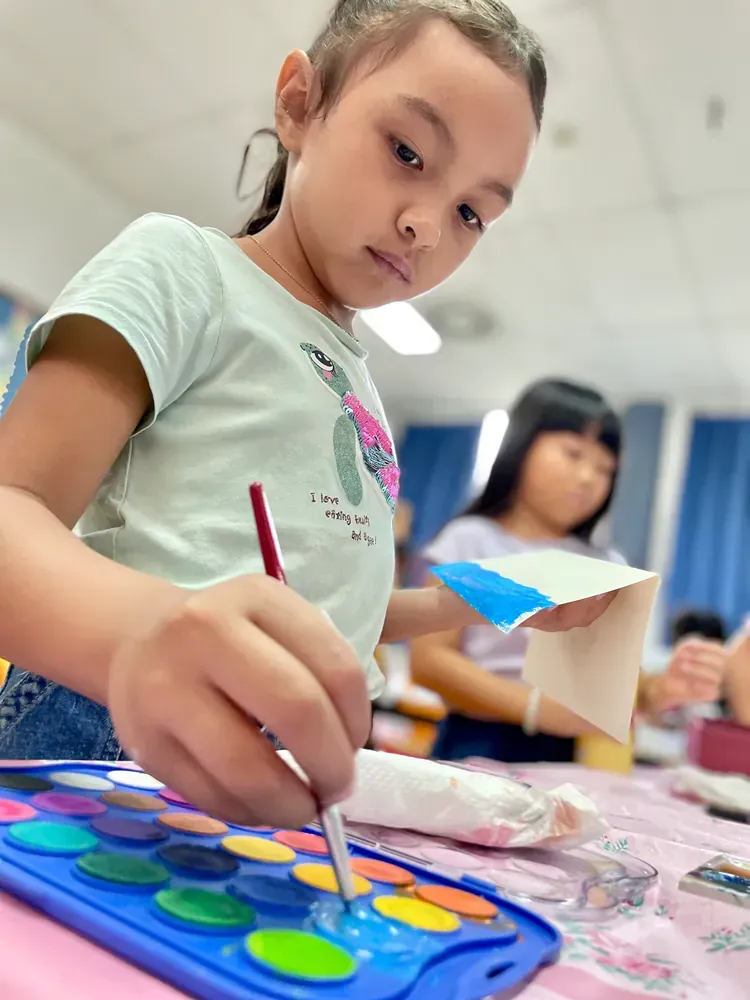 A little girl is painting with watercolors on a table.