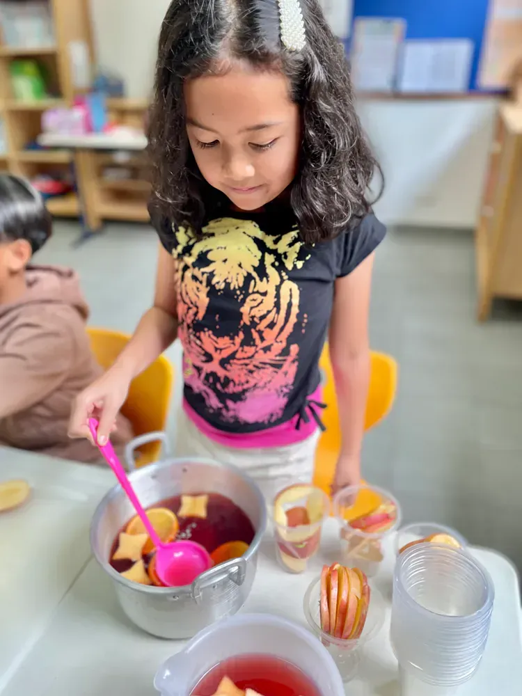 A little girl in a tiger shirt is pouring a drink into a bowl