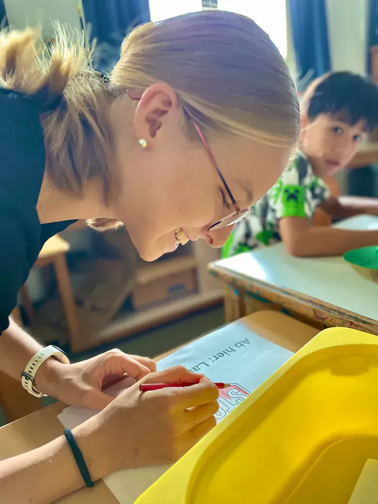 A woman is writing on a piece of paper in a classroom.
