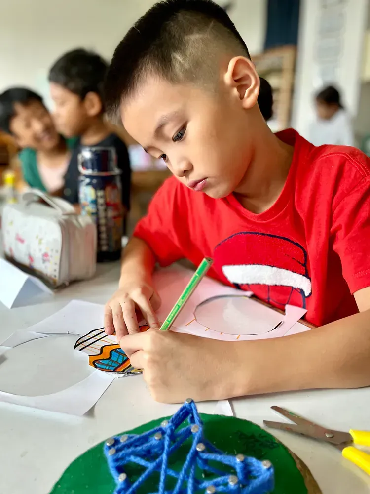 A young boy is sitting at a table drawing on a piece of paper.