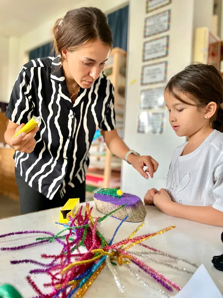 A woman and a little girl are sitting at a table making crafts.