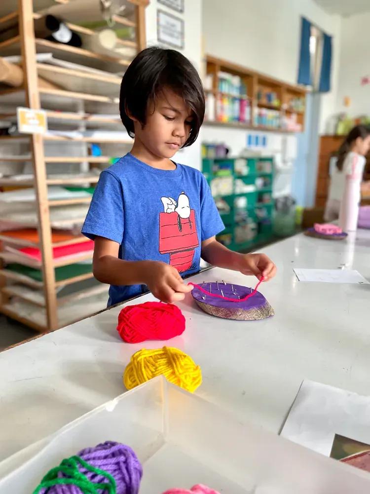 A young boy is sitting at a table playing with yarn.