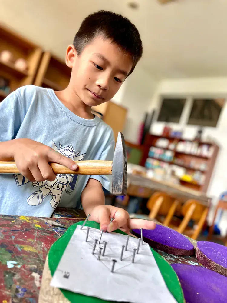 A young boy is using a hammer to hammer nails into a piece of paper.