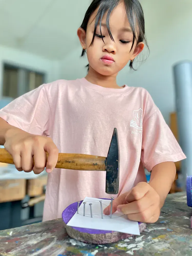 A little girl is holding a hammer over a piece of paper.