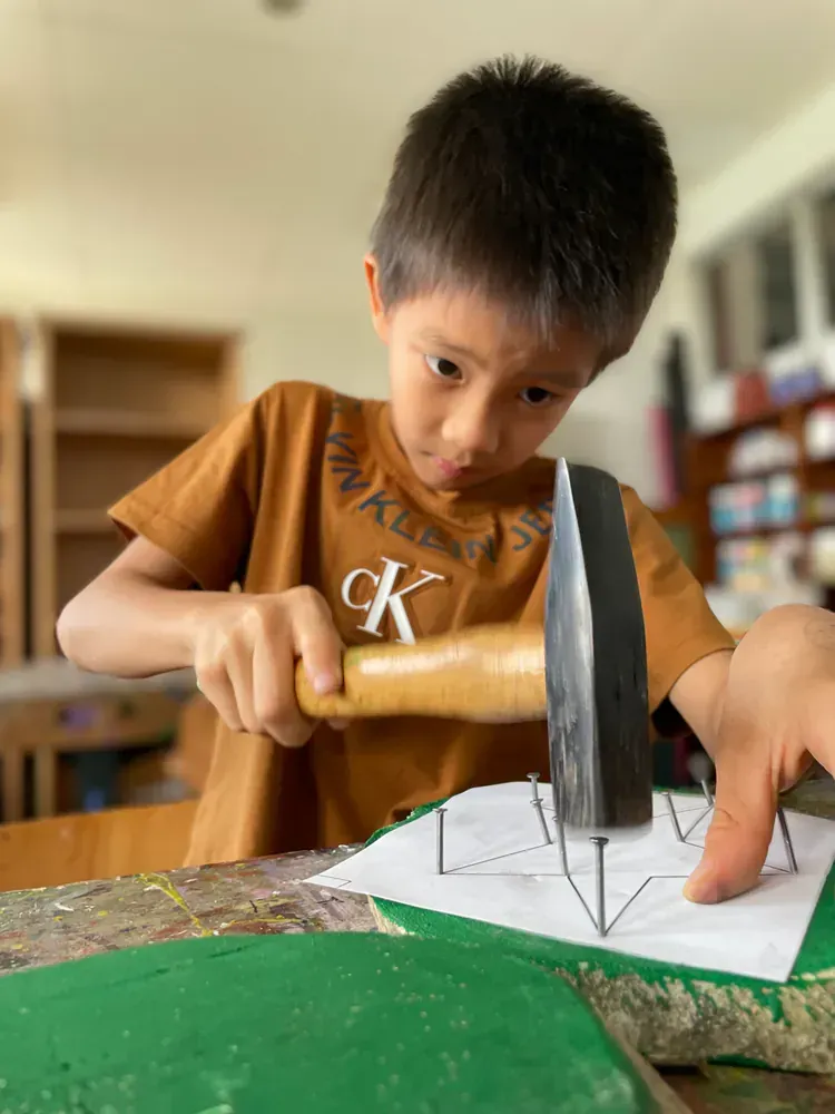 A young boy is hammering a nail into a piece of paper.