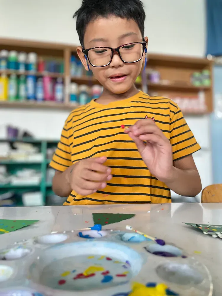 A young boy wearing glasses is sitting at a table playing with paint.