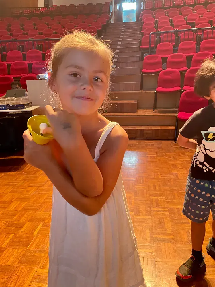 A little girl in a white dress is holding a yellow cup.