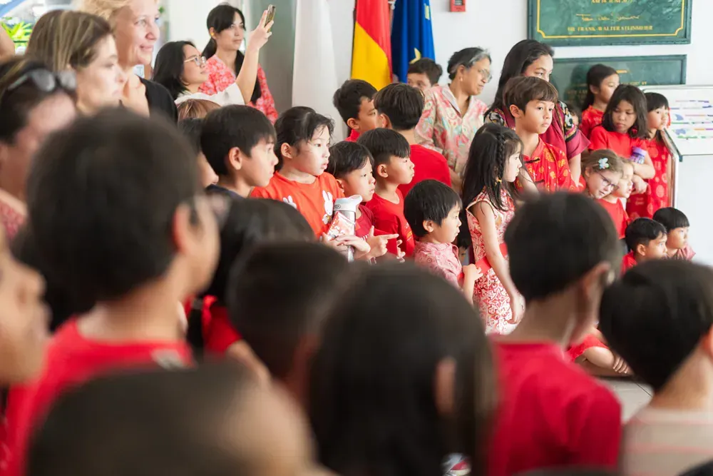 A large group of children in red shirts are sitting in a classroom.