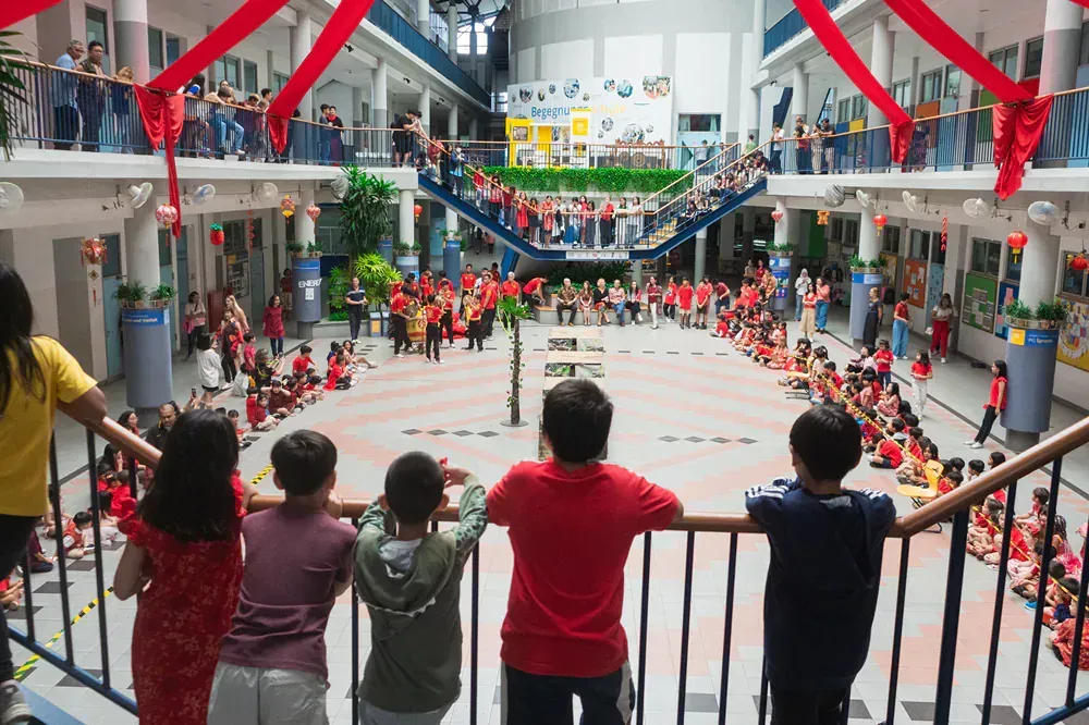 A group of children are standing on a balcony looking at a large group of people.