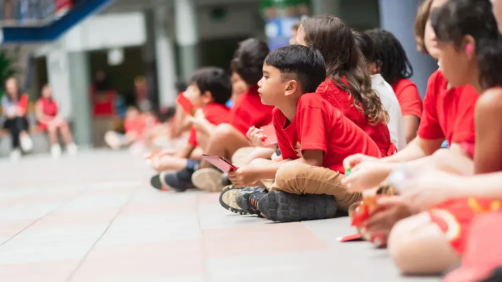 A group of children in red shirts are sitting on the ground.