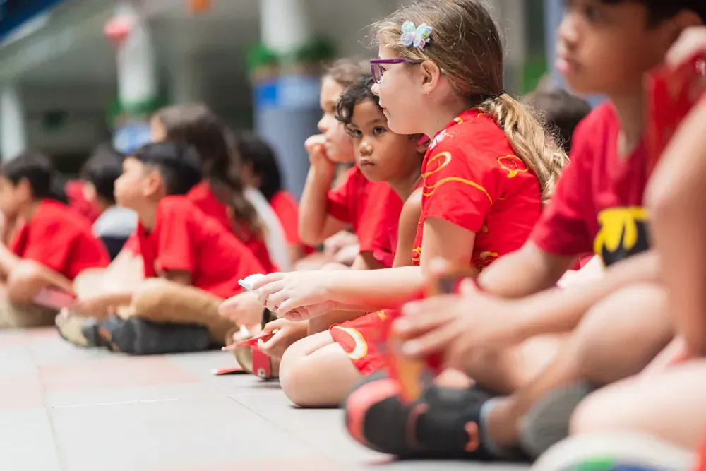 A group of children in red shirts are sitting on the ground.