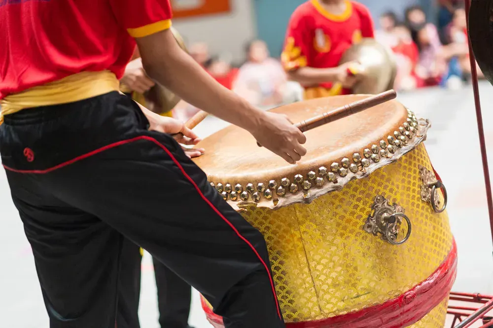 A person is playing a drum with wooden sticks.