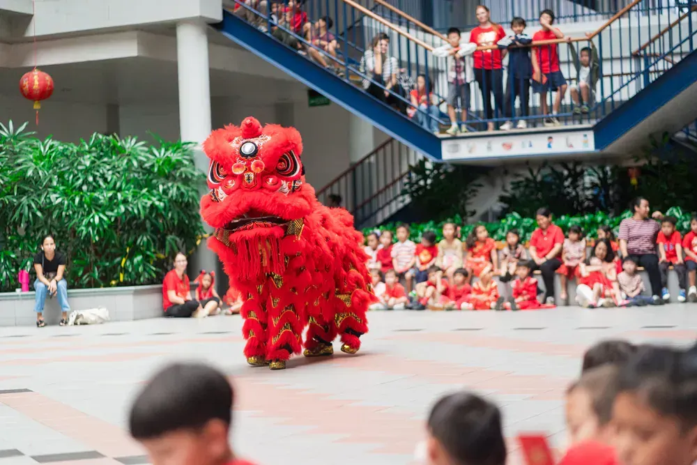 A group of children are watching a lion dance in front of a crowd.